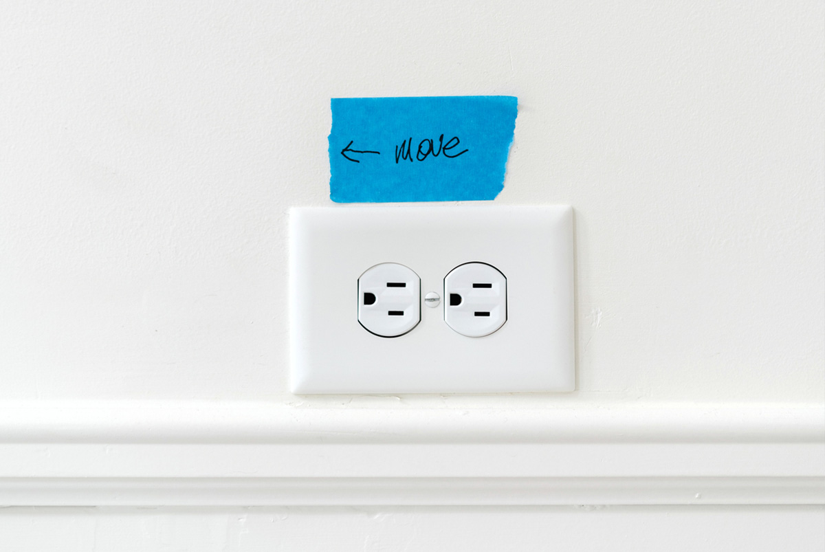 Close up of electrical outlet with piece of blue painter's tape above it that has 