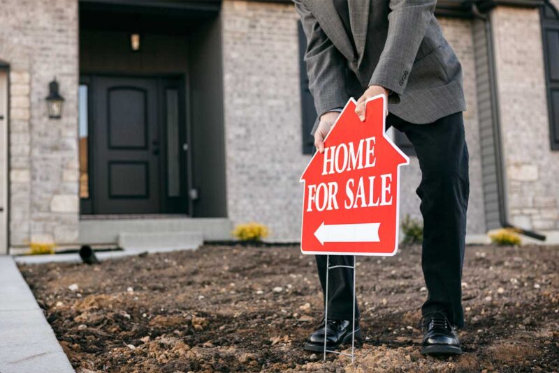 A listing agent puts a "for sale sign" in front of a home.