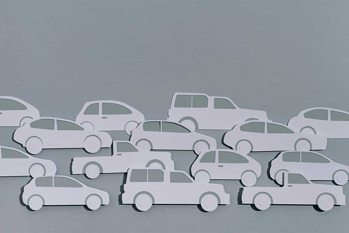 Gray background with several white paper car cutouts clustered together that resemble a busy road.