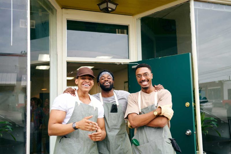 Three men wearing aprons standing outside of a building
