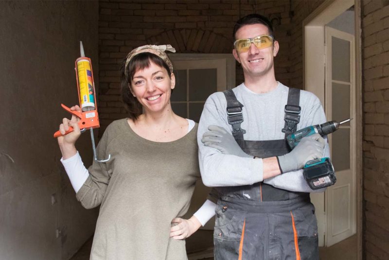 A woman and man in work clothes stand together during a home improvement project