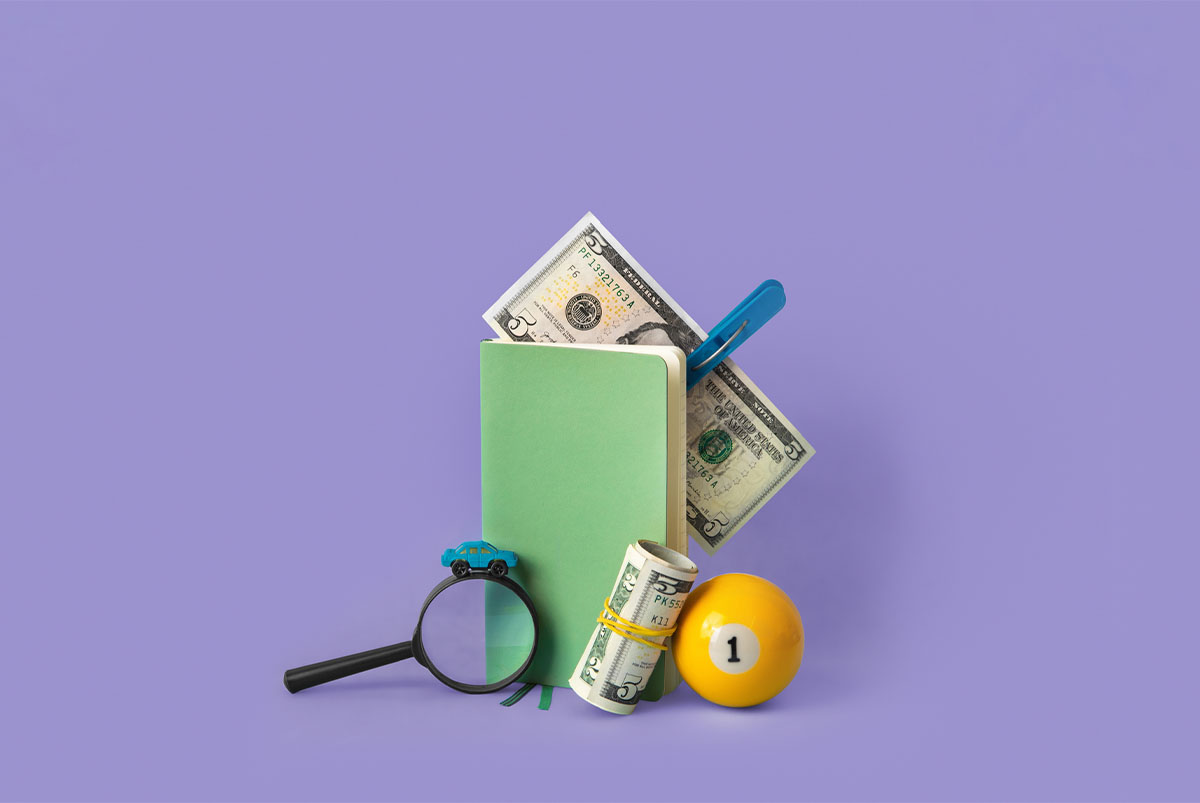 small objects (copy book, money, magnifying glass) on a purple background