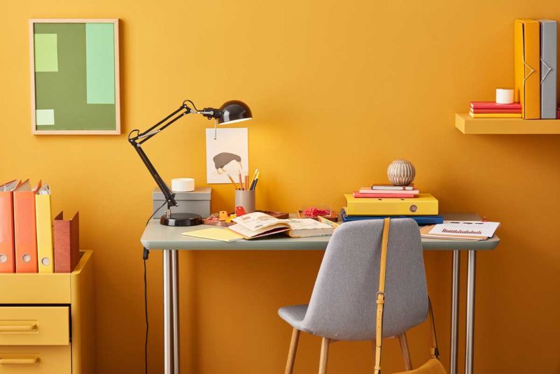 Cluttered desk in a yellow room.