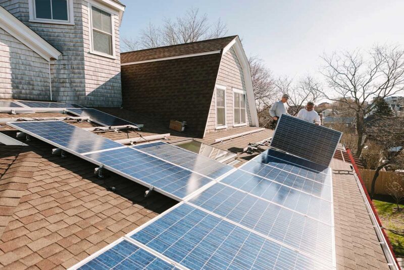 Workers install solar panels on the roof of a house.