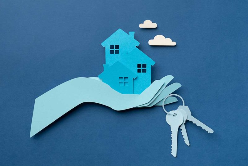Conceptual image with paper cut outs showing a hand holding a house in its palm with a set of keys dangling from its finger
