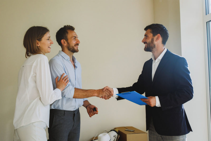 happy couple shaking hand with realtor who has blue folder