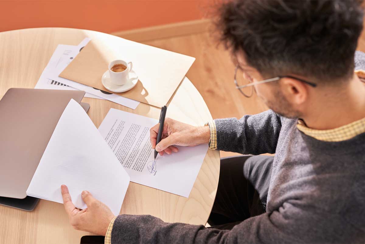 A man is signing a purchase agreement for a house while drinking coffee