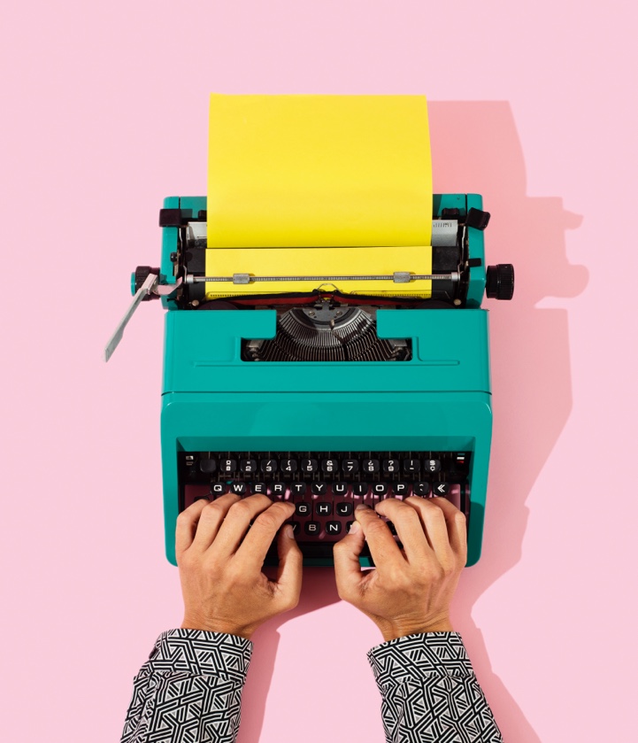 Hands typing on a teal typewriter with yellow paper